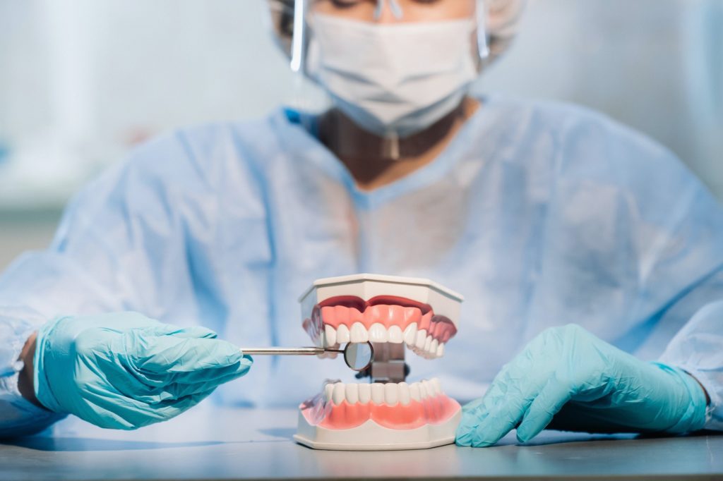 Coronas de Porcelana 3 a dental doctor wearing blue gloves and a mask holds a dental model