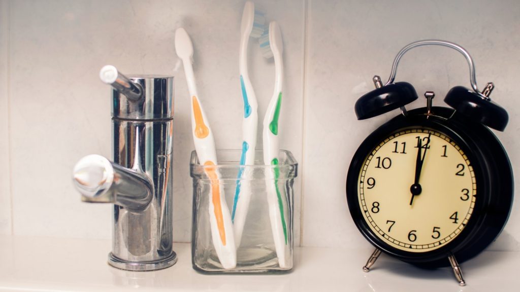 Blanqueamiento Dental Láser con Zoom 22 a toothbrushes in a glass container next to a alarm clock