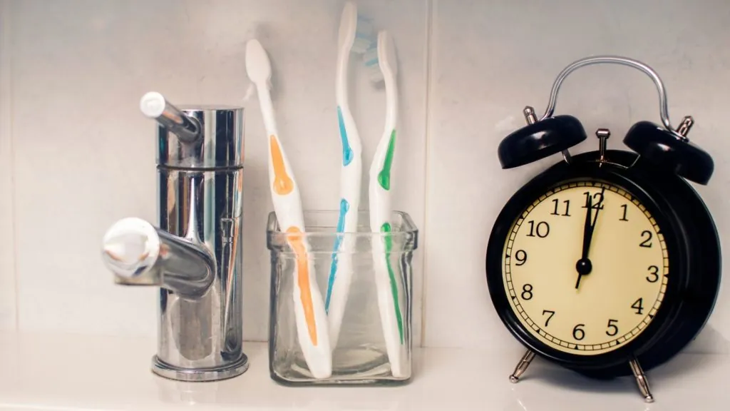 Blanqueamiento Dental Láser con Zoom 22 a toothbrushes in a glass container next to a alarm clock